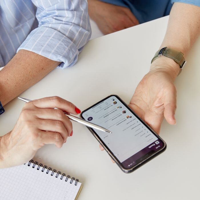 Two adults collaborate using a smartphone and a notepad in an indoor setting.